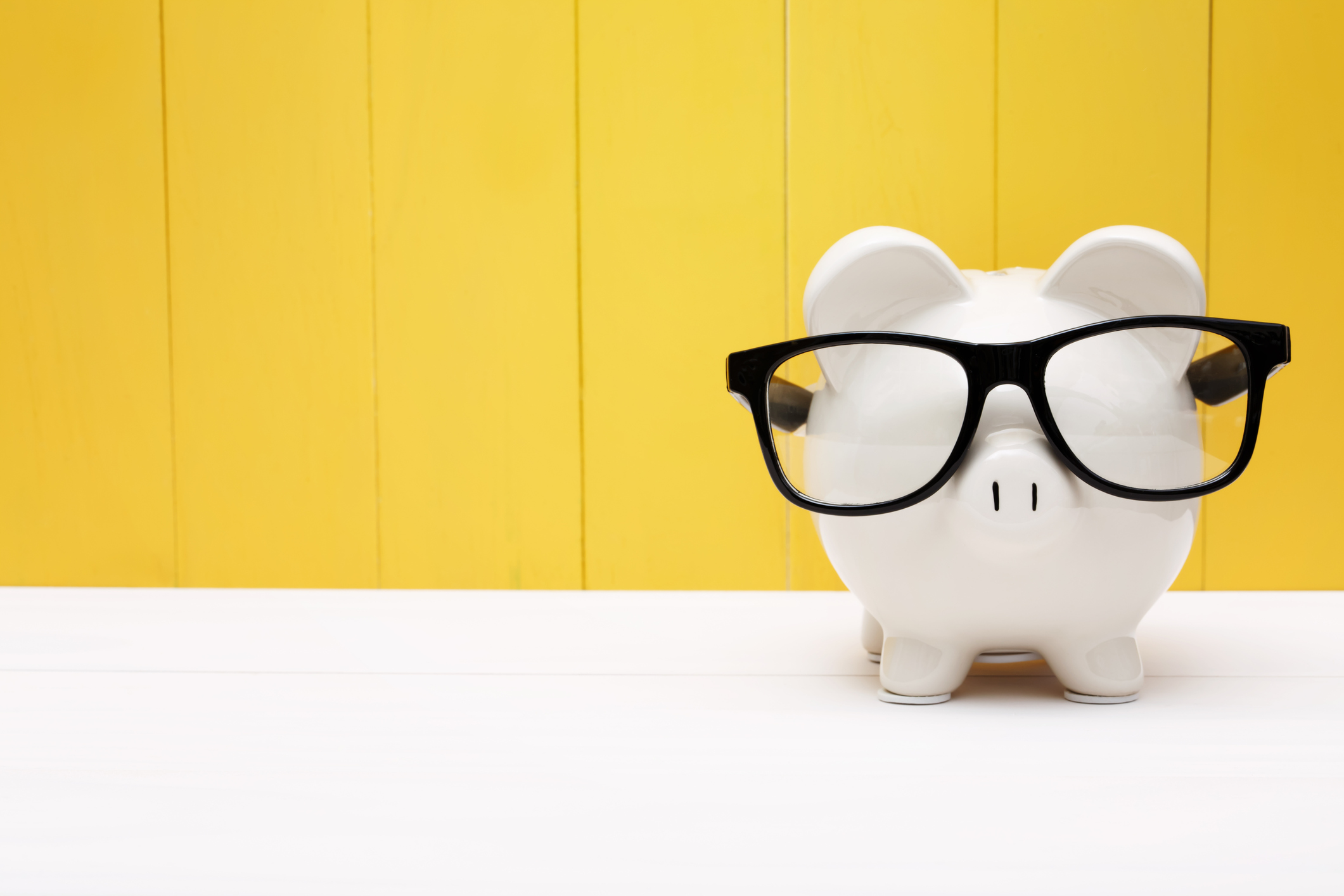 Piggy bank with glasses over yellow wooden wall