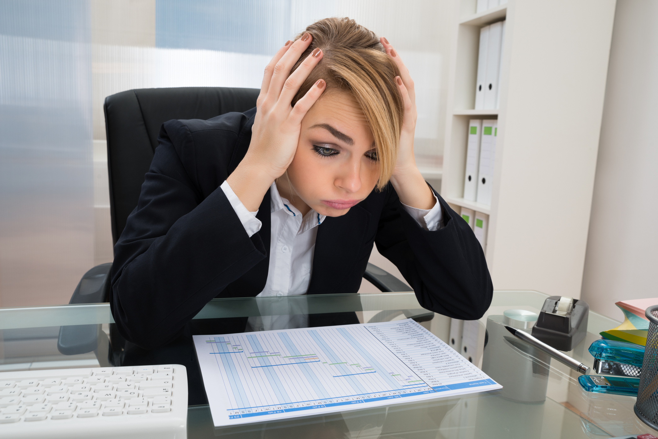 Portrait Of Stressed Businesswoman Sitting At Desk With Gantt Progress Chart